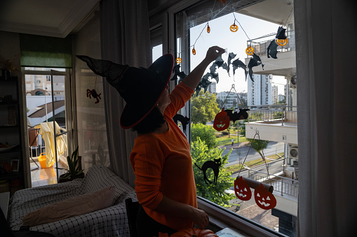 Photo of woman wearing witch's hat decorating home for Halloween in dusk. Shot in dark with a full frame mirrorless camera.