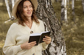 A young beautiful woman in a dress and hat stands and reads a Bible