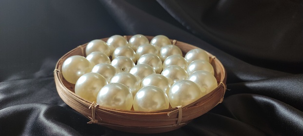 white synthetic pearls in a bamboo plate with a black background