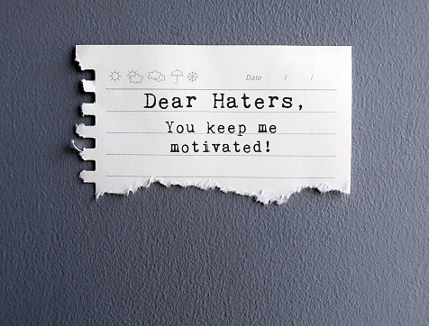 Yellow Note on grey wall with text THANK YOU HATERS , FOR BEING MY MOTIVATORS - Self reminder to stop let haters affect or take advantage of the situation but use them as fuel for success instead