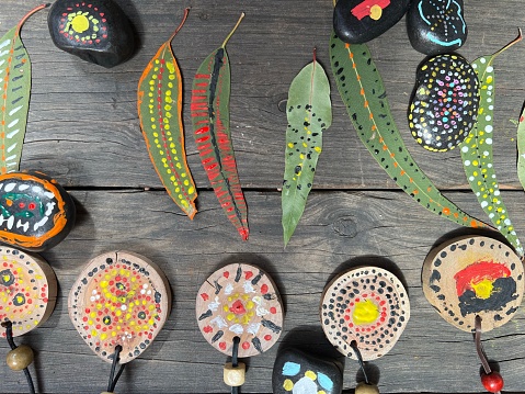 Horizontal high angle extreme closeup photo of painted patterned Eucalyptus leaves, decorated stones and painted wooden medallions on necklaces created during NAIDOC week elementary school activities celebrating Australian Indigenous History and Culture. Armidale, New England high country, NSW.