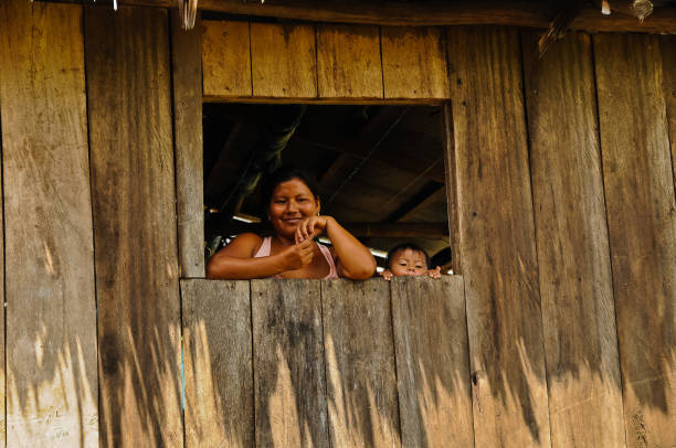 Pacaya-Samiria Nature Reserve, Amazon, Northeastern Peru, August 31, 2018\n\nMother and child peeping through a small window in their wooden hut on stilts, typical dwelling found in villages on the Amazon Rainforest.  The mother is saying her good-byes to visitors she and her family hosted for lunch. The toddler is reaching for the window sill to catch a glimpse of the visitors.