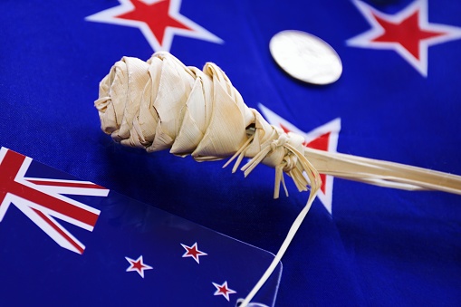 A background of New Zealand flags with a dried flower woven from New Zealand Flax plant leaves.