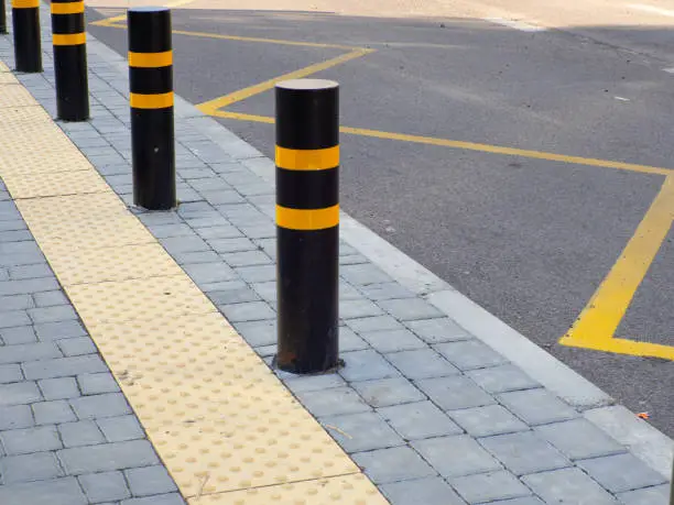 Yellow tactile pavement for the blind on the bus stop. Bus stop with traffic road bollards protecting pedestrian sidewalk. Concept traffic restriction, no access to drive. Yellow, black pillar bumper.