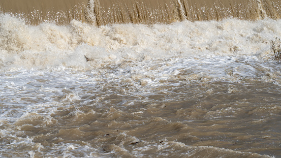 The river swollen after heavy rainfall and flood water crashing through valley. The water flows fast from the high valley to the plain. General contest of a river in flood