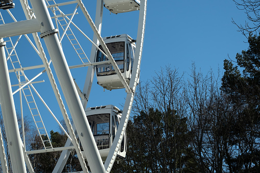 Fragment of the Ferris wheel. White cabins on blue sky and early spring park trees.