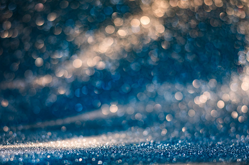 Bokeh glitter texture glowing with warm lights in the cold darkness. New Year and other holidays party background.
