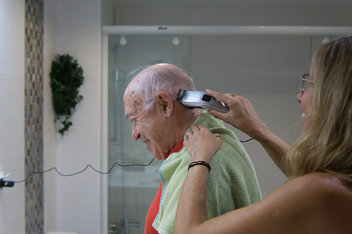 Funny family home care cutting the hair of an elderly person in the bathroom at home.