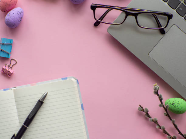 istock Work desk with devices and easter holiday multicolored eggs on pink background 1698300800