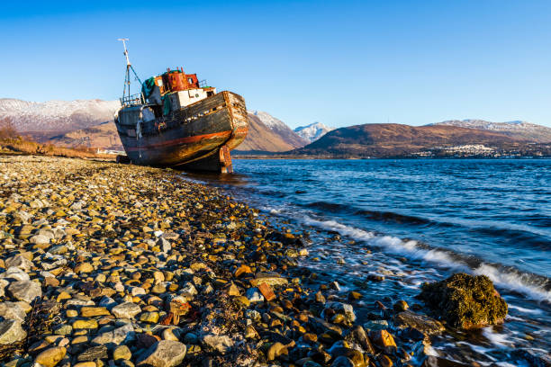 Old abandoned fishing boat wreck situated by the shores of Loch Linnhe at Corpach on the west coast of Scotland, with Ben Nevis and the Nevis range in the background.