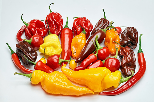 Top view close up of a bowl full of chilli powder beside two chilli peppers isolated on white background. Predominant color is red. Studio shot taken with Canon EOS 6D Mark II and Canon EF 100 mm f/ 2.8