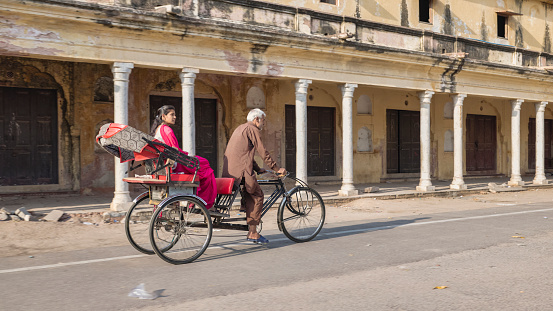 Indian man riding his bicycle rickshaw with a female customer on streets of Rajasthan, India.