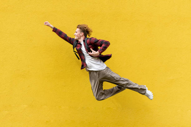 young guy student with backpack flies forward and hurries to study, man in superman pose jumps and runs in the air