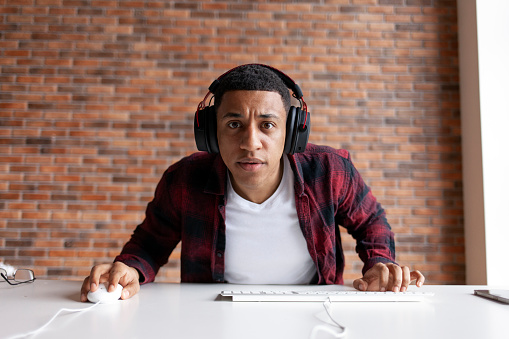 guy african american gamer in headphones sits at computer desk and plays video game at home, the man is focused on the game