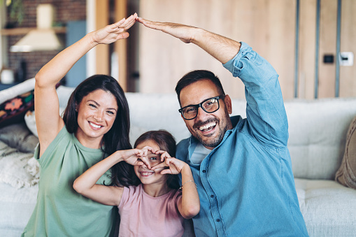 Portrait of smiling father, mother and daughter making heart and house signs