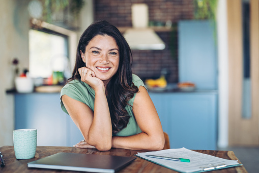 Smiling woman with laptop and coffee mug in a domestic kitchen