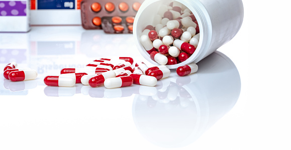 Red and white capsules pill spilled out from white plastic bottle. Prescription drug. Healthcare and medicine. Antibiotics drug. Antimicrobial capsule pills. Pharmaceutical industry. Pharmacy product.