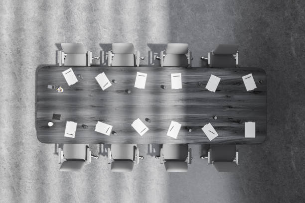 Multiple gray, modern, leather chairs pushed into a brown, wooden conference table in a brightly lit white room.