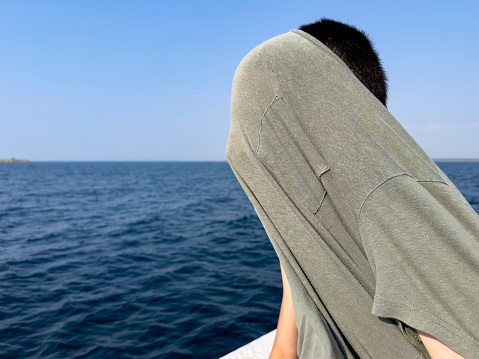 The boy is traveling on a boy cruise ship in the North Aegean Sea. Thoughtful and happy. Sunny summer day. Traveling background. Tourism concept.
