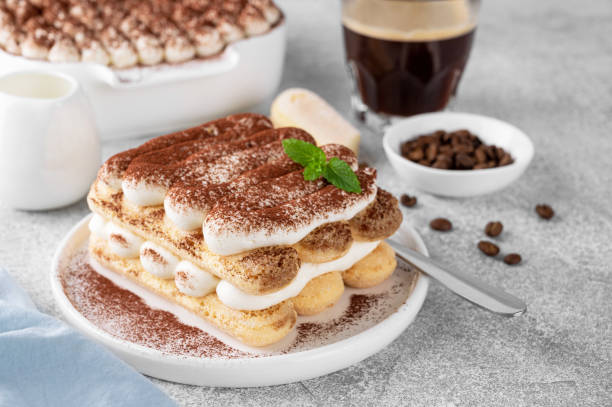 istock Tradition italian layered dessert tiramisu with mascarpone cream and biscuits on a white plate with cup of coffee on a gray concrete background. 1698433643