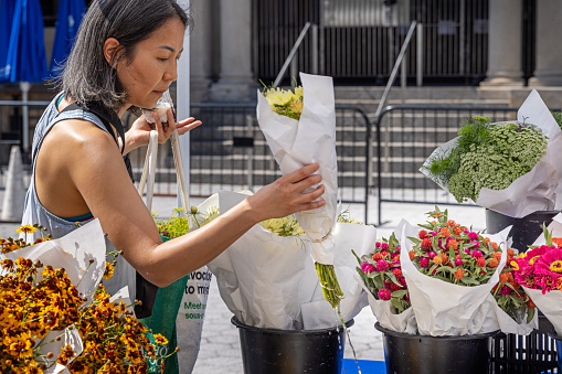 Union Square, Manhattan, New York, USA - August 11th 2023:  Asian woman looking at bouquets at a flower stall at a farmers market