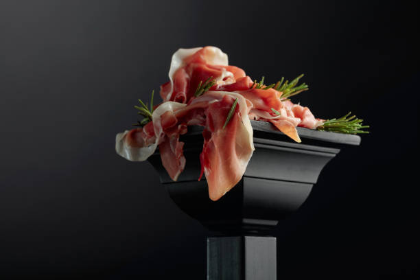 Prosciutto with rosemary on a black podium.