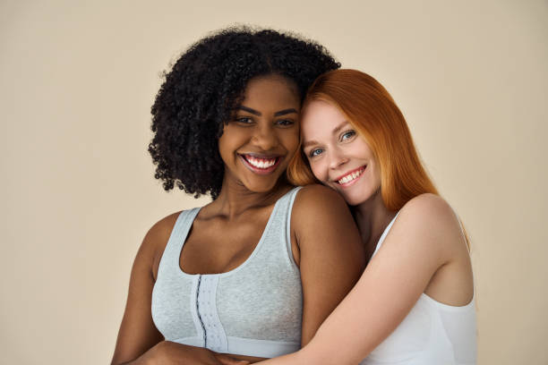 Two happy diverse young girls hugging isolated on beige background, portrait. Two happy diverse women, African and Caucasian young girls friends multiethnic models hugging smiling looking at camera standing isolated on beige background. Diversity and beauty concept, portrait. diverse models stock pictures, royalty-free photos & images