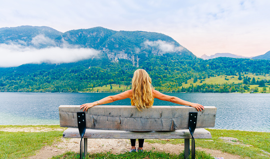 Woman sitting on bench looking at lake- relax, vacation,serene people concept