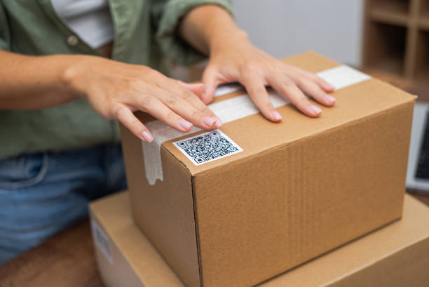 istock E-commerce: Woman hands apply QR code sticker to package, symbolizing online shopping and shipping. 1698539406