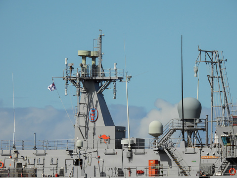 The superstructure and bridge of HMAS Choules, a supply and transport vessel of the Royal Australian Navy docked at Garden Island in Sydney Harbour.  In the far distance is a large bank of clouds.  This image was taken on a sunny afternoon on 23 September 2023.