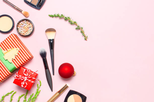istock Various cosmetic products for make-up, blusher, powder, brushes, lipstick, eyeshadow and Christmas gift, fir branches, red ball on pink background Flat lay top view New year concept, winter decoration 1698592166
