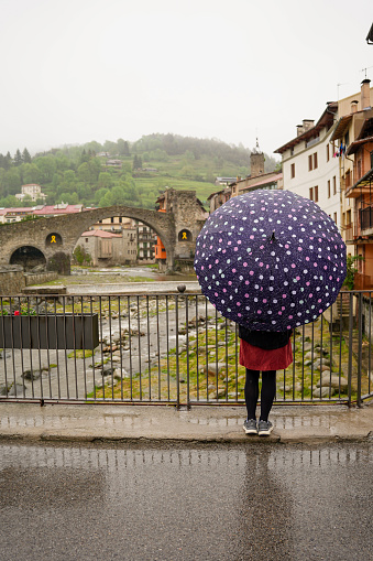 woman tourist protecting herself from the rain with an umbrella in wintertime in Camprodon. Bad weather. Rear view