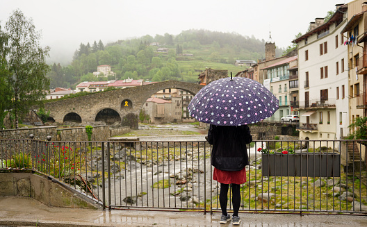 woman tourist protecting herself from the rain with an umbrella in wintertime in Camprodon. Bad weather. Rear view