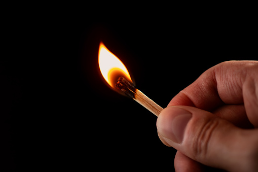 Hand holding burning match stick. Photo on a black background.