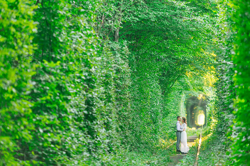 a tree tunnel and a railroad track. the couple in love stand face to face