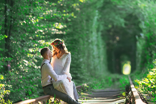 a couple in love sits on a railroad on the background of a tree tunnel