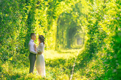 a couple embracing and looking at each other in a tunnel of trees. railway