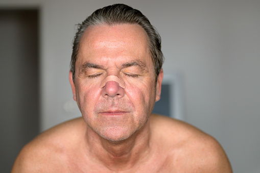 Portrait of a middle aged man with a nose tape and eyes closed standing in the bedroom