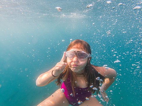 A girl is snorkeling, fully submerged in water and surrounded by airbubbles. The sea or ocean water is in beatyfull blue color.
