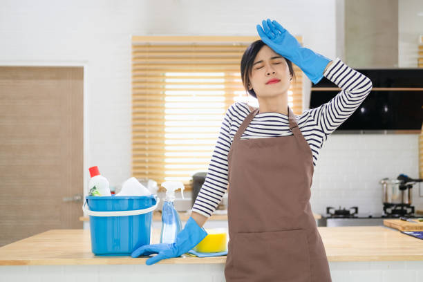 mulher jovem cansada de pé na sala de cozinha com produtos de limpeza e equipamentos, conceito de trabalho doméstico - home interior women domestic kitchen cabinet - fotografias e filmes do acervo