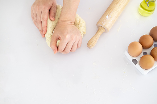 Top view of Hands kneading dough on white table, closeup, Flat lay. Woman kneading dough on table sprinkled with flour.Making bakery by female hands at home.