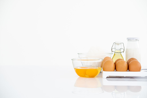 Wheat flour with eggs, oil and milk on table . White table Front view copyspace