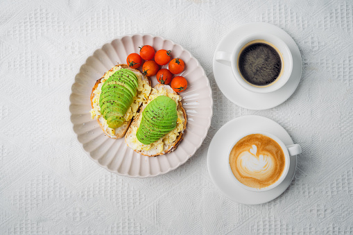 Scrambled eggs on toast with avocado and tomato with hot coffee
