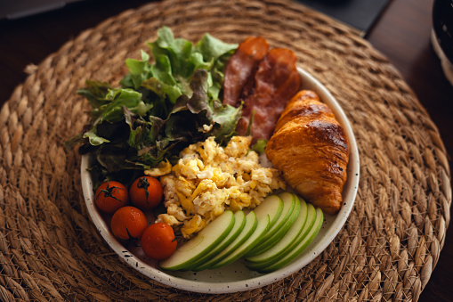 Breakfast Croissant, Scrambled Eggs, Bacon with Avocado and Tomato Salad On the work desk with laptop