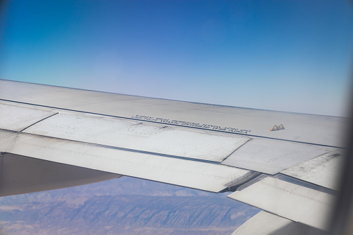 A wing of the airplane flying over mountains on a clear day with blue sky, with \
