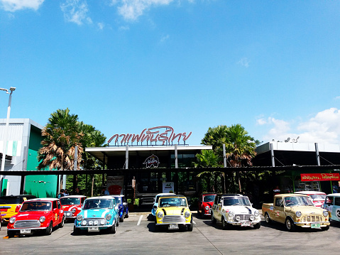 Nakhon Ratchasima, Thailand - September 22, 2023: Colorful classic Mini Austin Cooper parking on street in front of Thai coffee shop with building and blue sky background. Small vehicle, Vintage car