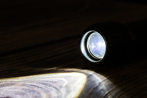 Black led operational flashlight on rough wooden surface - closeup with selective focus.