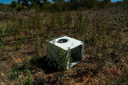 Abandoned washing machine in the middle of a field, a stark reminder of improper waste disposal.
