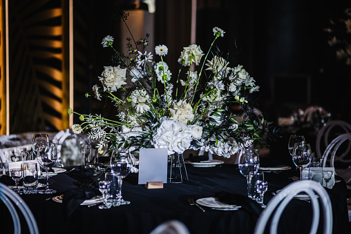 Wedding setup, dinner table reception in area on party. Festive decor with flower composition, candles on black tablecloth. Banquet decoration in hall restaurant. Setting. Birthday, baptism, event.