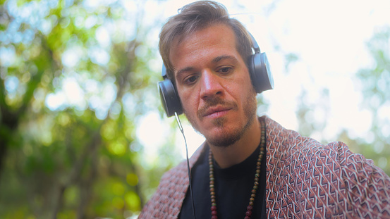 A close-up portrait of a man focusing on making music in a public park.